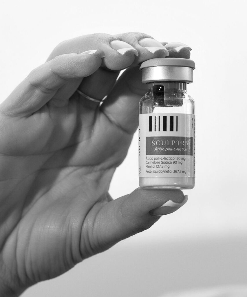 Hand holding closed vial between thumb and fingers, label title reads Sculptra, black and white